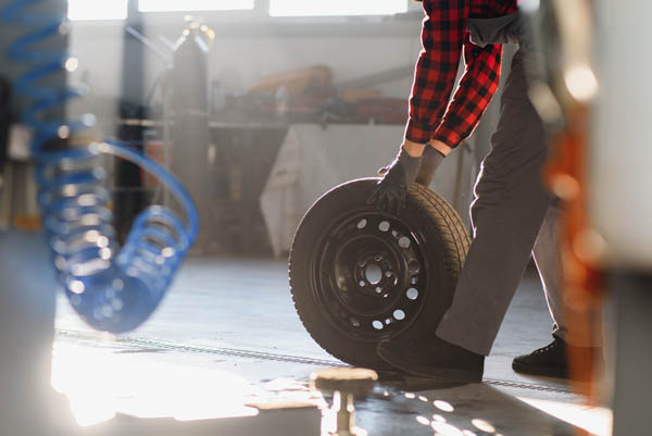 Mechanic Holding A Tire Tire At The Repair Garage. Replacement Of Winter And Summer Tires. Imagen de Mechanic Holding A Tire Tire At The Repair Garage. Replacement Of Winter And Summer Tires.