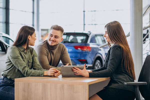 Young Couple Talking To A Sales Person In A Car Showroom Imagen de Young Couple Talking To A Sales Person In A Car Showroom